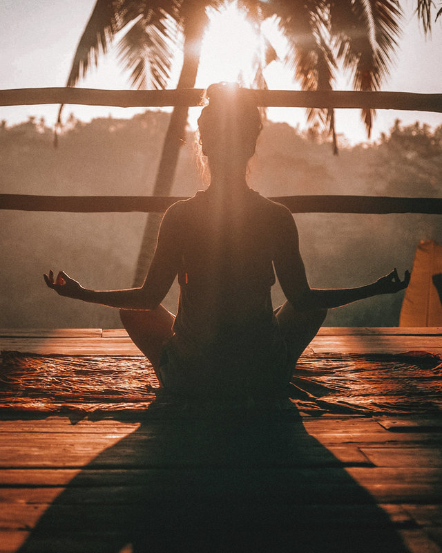 Person meditating on a deck at sunrise